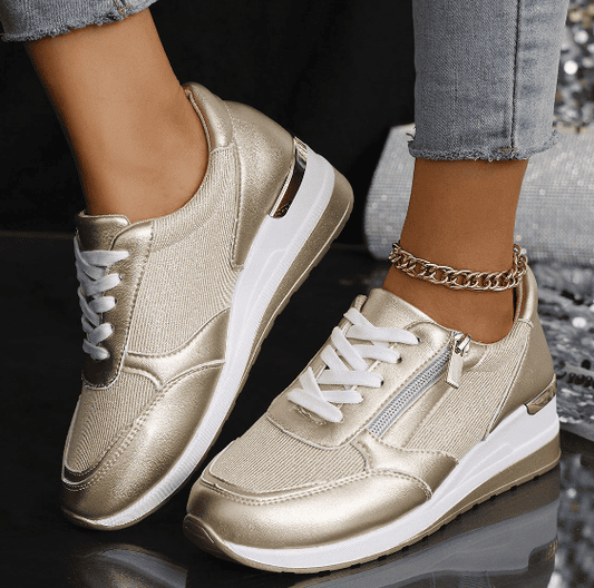 Gold sneakers with white soles worn by a person on a reflective surface.