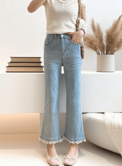 Person wearing light blue jeans with lace cuffs in a minimalistic room.